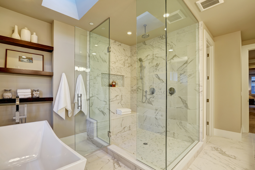 Modern bathroom with marble tile, glass shower, and freestanding tub, showcasing the warmth and comfort of radiant floor heating.