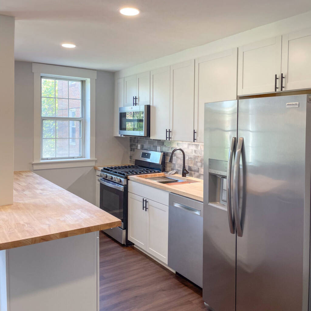 view of a kitchen with stainless steel appliances, white counters, a tan butcher block style counter, and dark wood floors with natural light coming in and recessed can lights