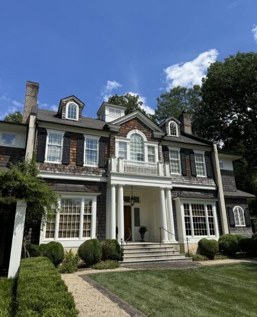 A substantial house with an extensive porch and a wide lawn in the foreground.
